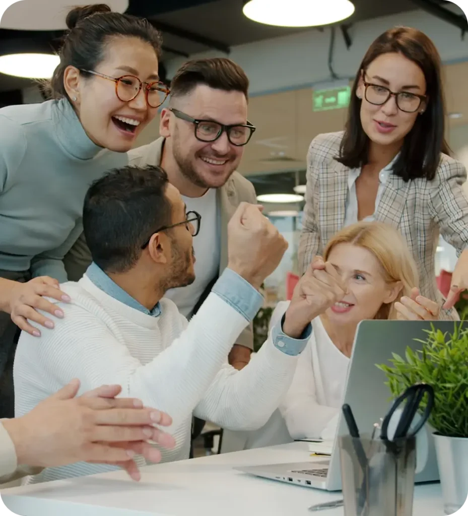 Een enthousiaste groep collega's viert gezamenlijk succes rond een laptop in een kantooromgeving.